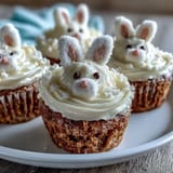 Saftige Karottenkuchen-Muffins mit cremiger Frischkäse-Frosting, dekoriert als niedliche Osterhasen für festliche Frühlingsfeiern.