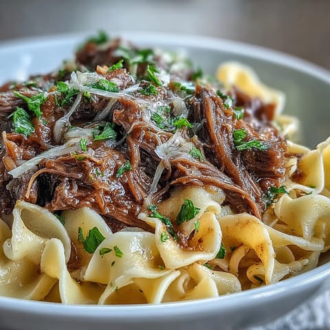 Langsam gegartes Rindfleisch in würziger Brühe mit Zwiebeln auf Butter-Eiernudeln angerichtet