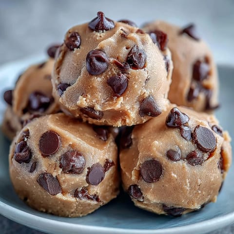 Zu 100 % pflanzliche Vegan Chickpea Cookie Dough Bites mit dunklen Schokoladenstückchen auf einer rustikalen Holzplatte